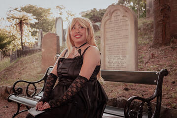 Pōhutukaryl Cosplay as Misa Amane, sitting on a bench with her Death Note, smiling into the distance